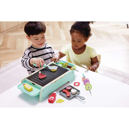 Two children playing with a toy grill set on a light-colored surface.